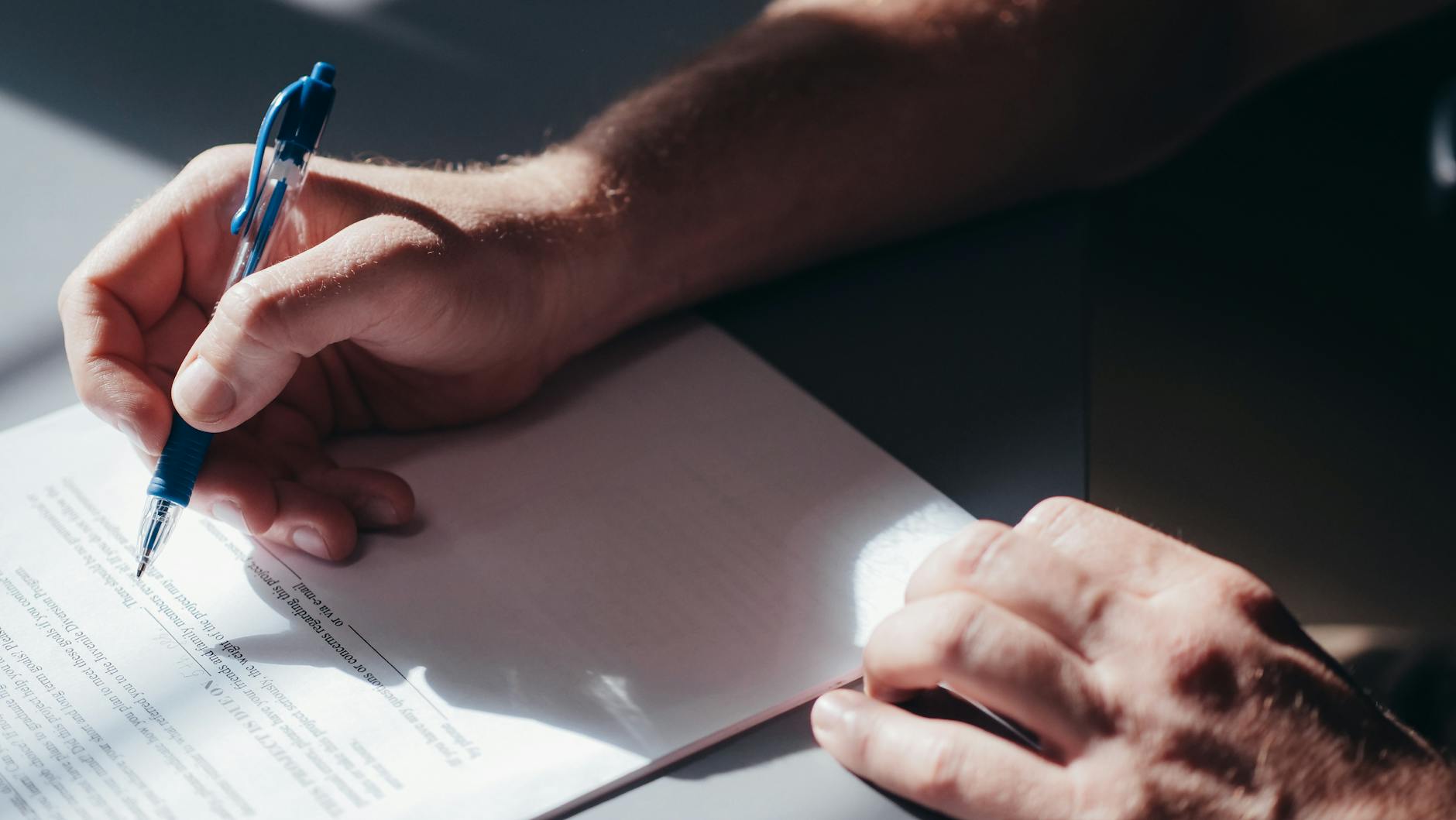 A contractor signing release paperwork at a desk on a construction job site, hard hat and project plans nearby