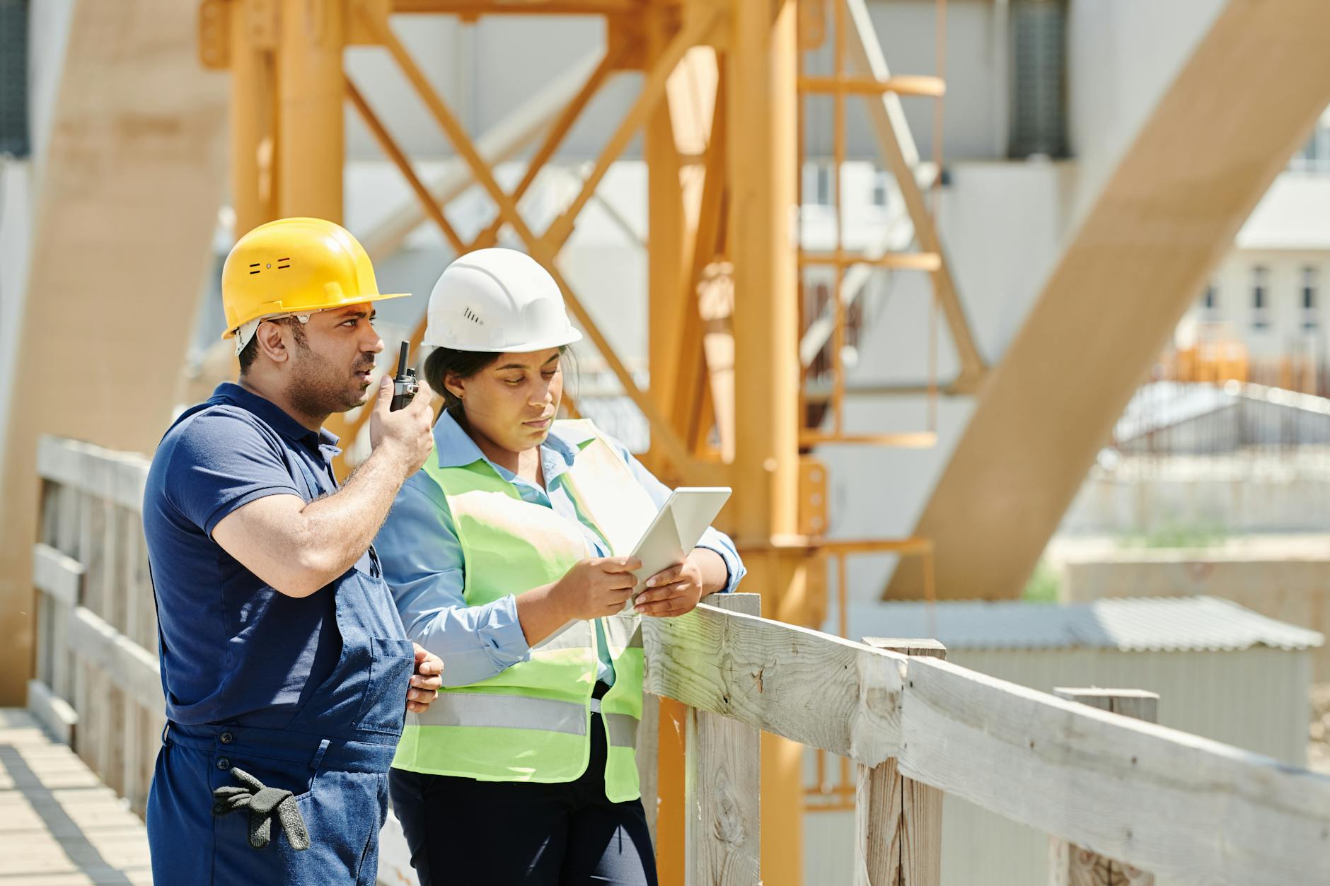 General contractor in a hard hat reviewing plans on a construction site with subcontractors working in the background