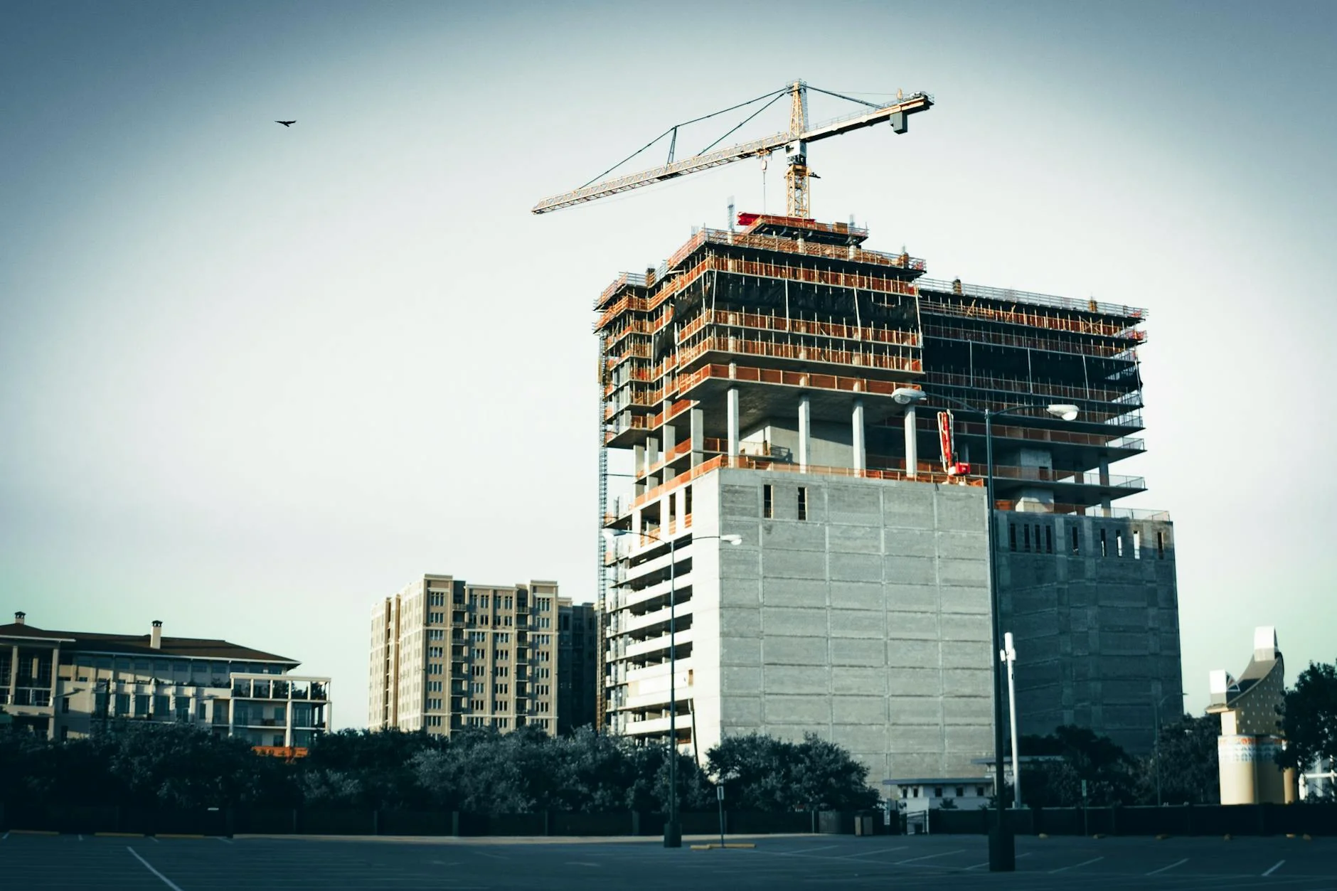 A multi-story commercial building under construction in Texas with a tower crane on top, viewed from a wide parking lot